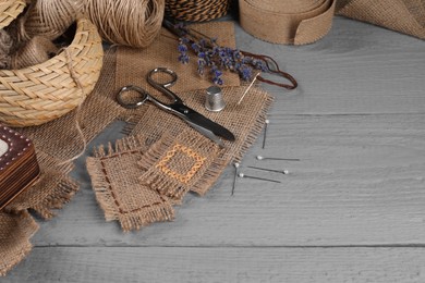 Photo of Pieces of burlap fabric with different stitches and sewing tools on grey wooden table, space for text