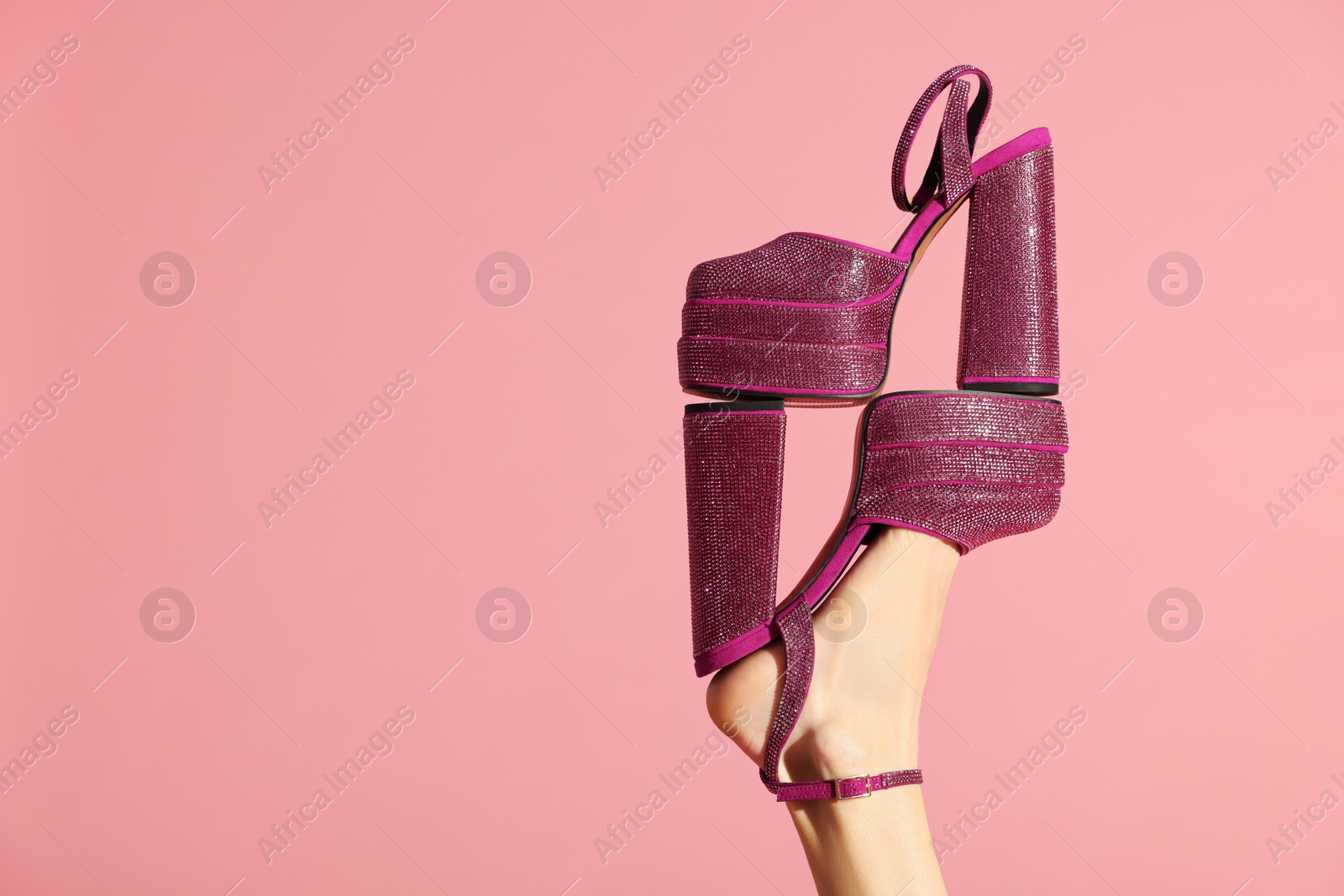 Photo of Stylish presentation. Woman wearing high heeled shoe with platform and square toes holding another one on pink background, closeup. Space for text