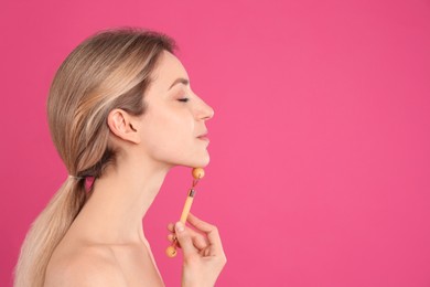 Young woman using natural jade face roller on pink background, space for text