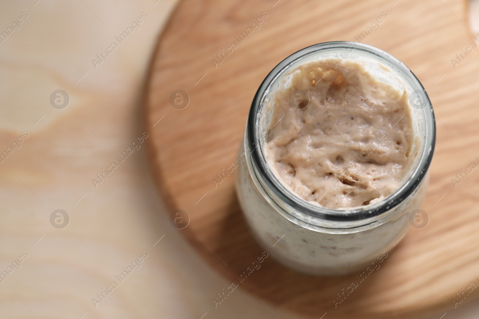 Photo of Sourdough starter in glass jar on wooden table, top view. Space for text