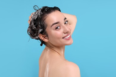 Portrait of beautiful happy woman washing hair on light blue background