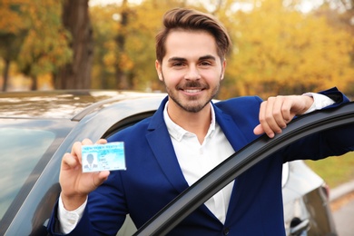 Young man holding driving license near open car