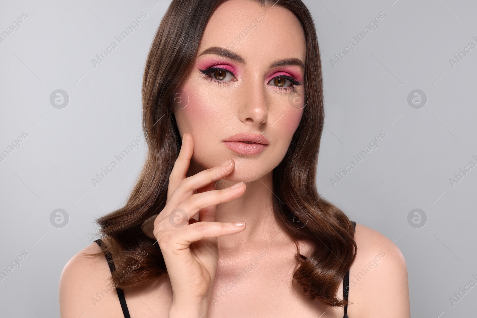 Photo of Portrait of beautiful young woman with makeup and gorgeous hair styling on light grey background