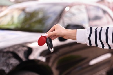 Woman holding car flip key near her vehicle outdoors, closeup