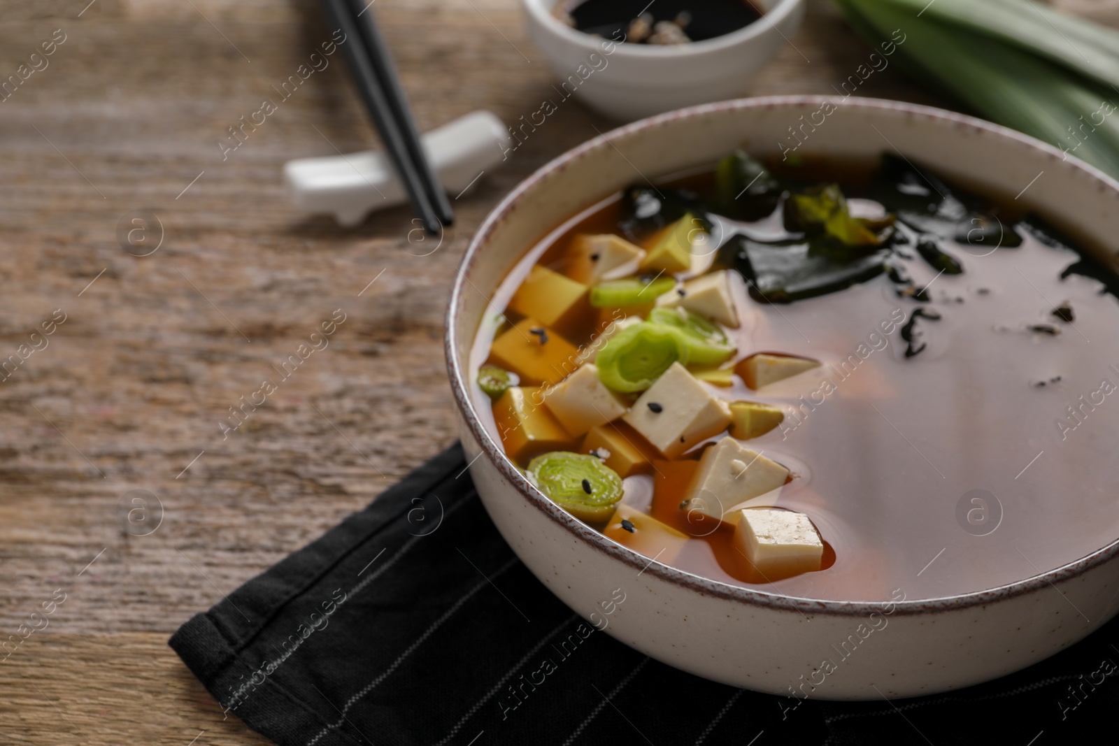 Photo of Bowl of delicious miso soup with tofu on wooden table, closeup. Space for text