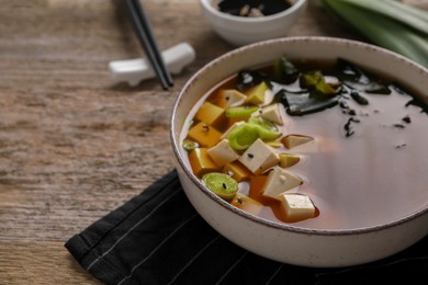 Bowl of delicious miso soup with tofu on wooden table, closeup. Space for text