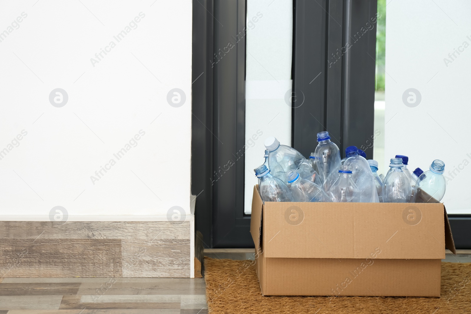 Photo of Cardboard box with used plastic bottles near entrance door in hallway. Recycling problem