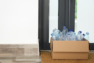 Cardboard box with used plastic bottles near entrance door in hallway. Recycling problem