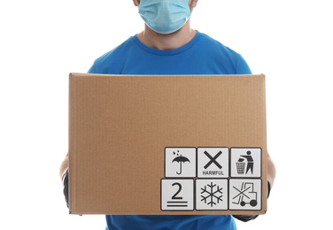 Photo of Courier holding cardboard box with different packaging symbols on white background, closeup. Parcel delivery