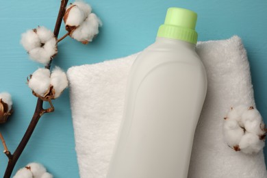 Photo of Bottle of fabric softener, terry towel and cotton flowers on light blue wooden table, flat lay