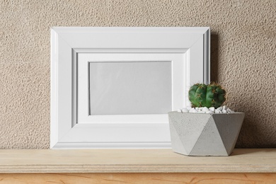 Photo of Blank frame and succulent plant on wooden table near brown wall, space for design. Home decor
