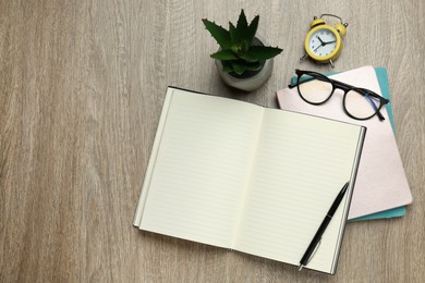 Photo of Notebooks, glasses, pen, alarm clock and houseplant on wooden table, flat lay. Space for text