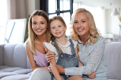 Photo of Young woman with mature mother and little daughter in living room