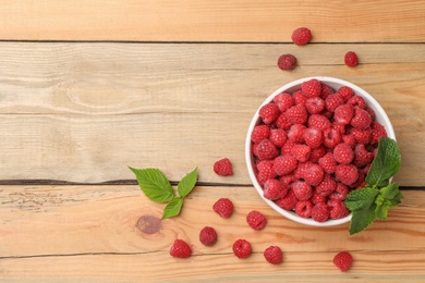 Photo of Bowl with ripe aromatic raspberries on wooden table, top view