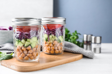 Photo of Healthy salad in glass jars on white wooden table. Space for text