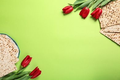 Tasty matzos and flowers on green background, flat lay with space for text. Passover (Pesach) Seder