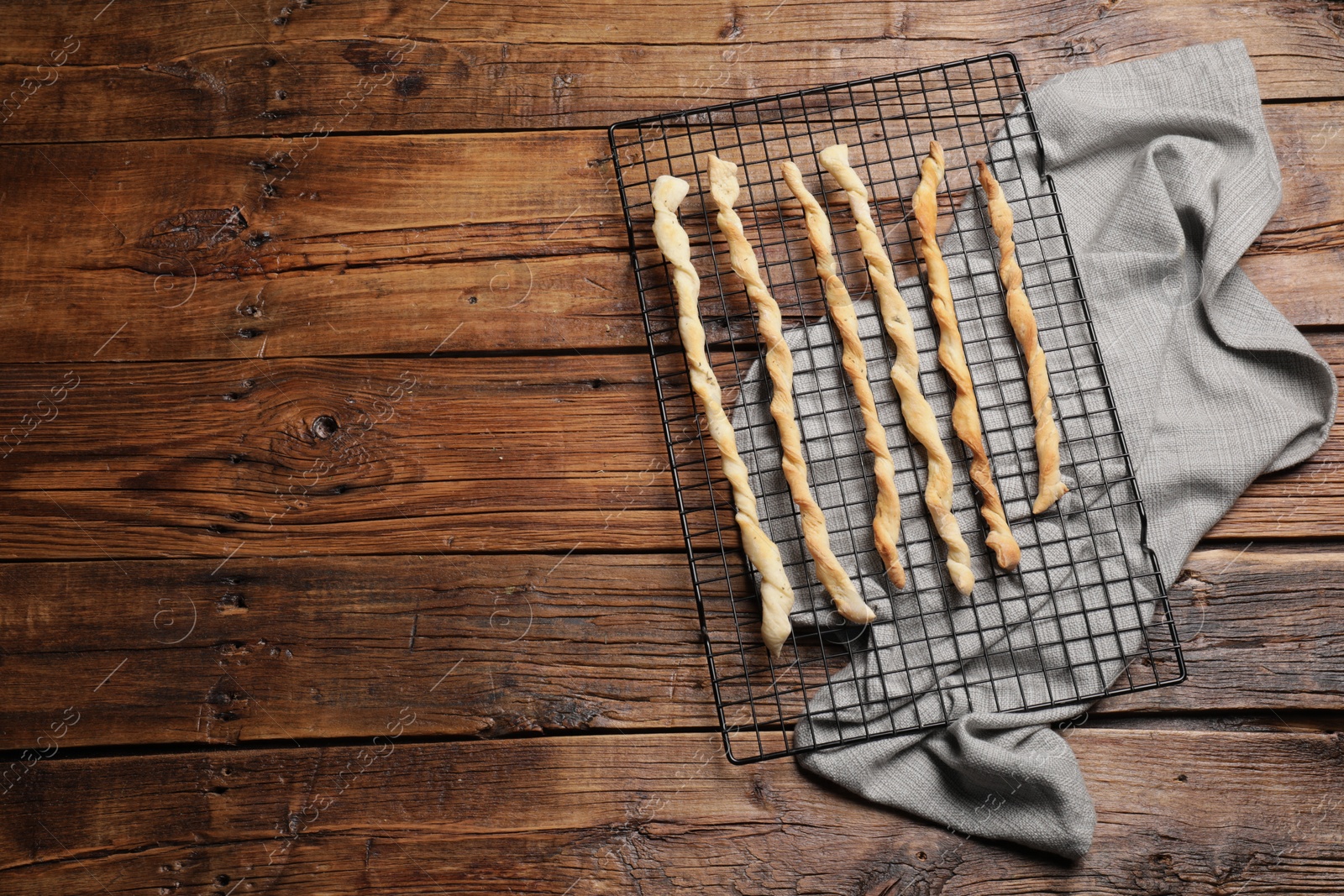 Photo of Rack with homemade breadsticks on wooden table, top view and space for text. Cooking traditional grissini