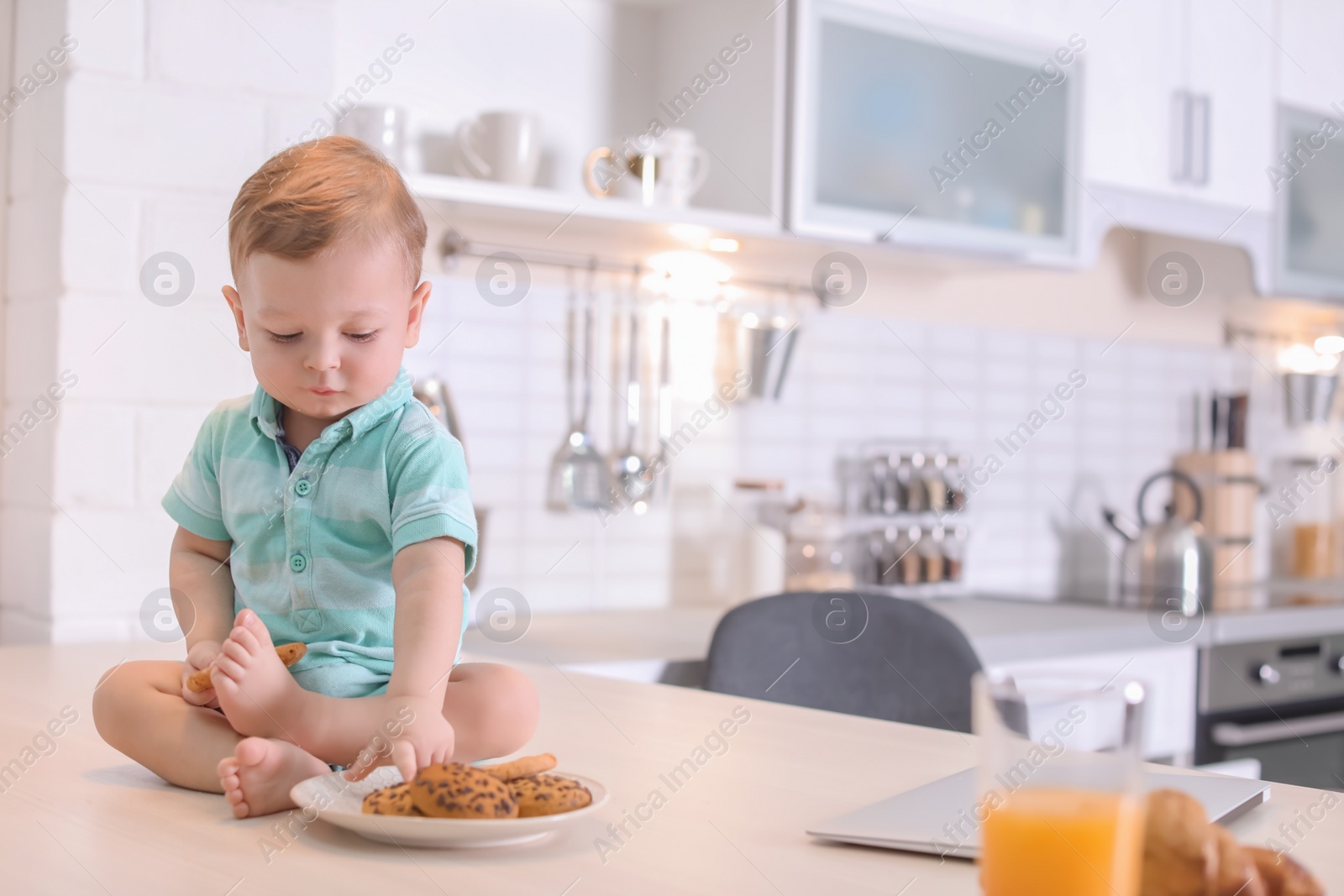 Photo of Cute little boy with cookies sitting on table in kitchen