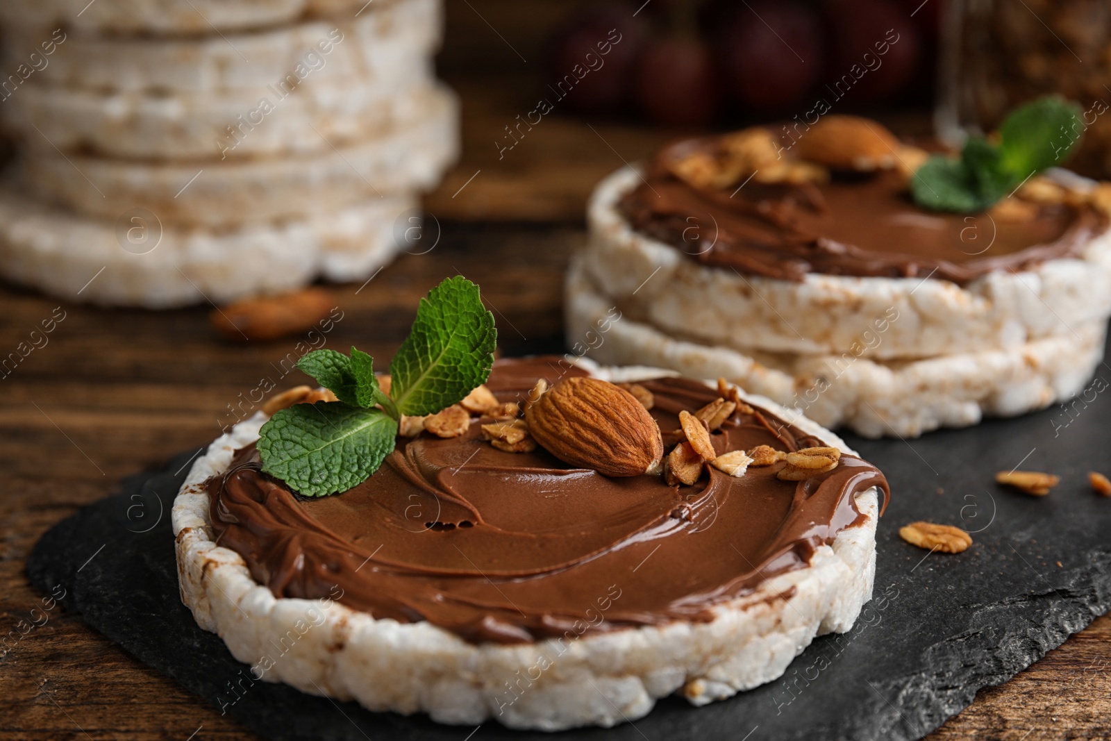 Photo of Puffed rice cakes with chocolate spread, nuts and mint on wooden table, closeup