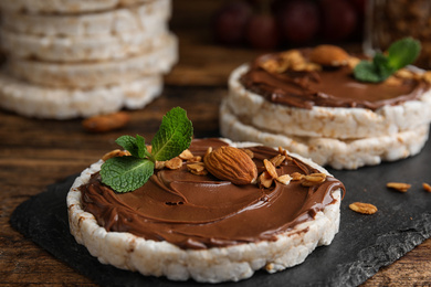 Photo of Puffed rice cakes with chocolate spread, nuts and mint on wooden table, closeup
