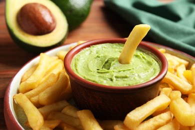 Photo of Plate with french fries, guacamole dip and avocado served on wooden table, closeup