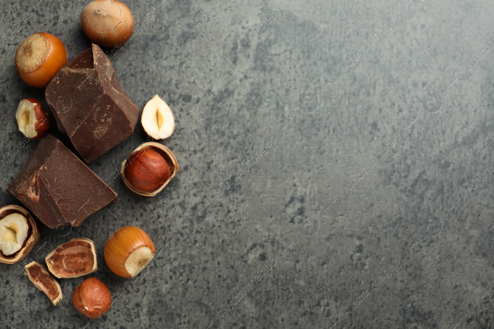 Photo of Delicious chocolate chunks and hazelnuts on grey table, flat lay. Space for text