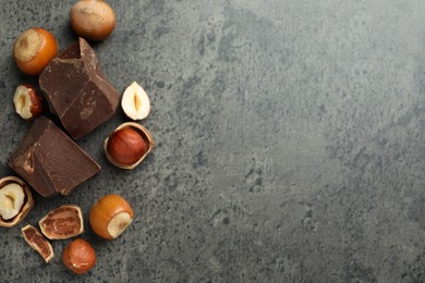 Delicious chocolate chunks and hazelnuts on grey table, flat lay. Space for text