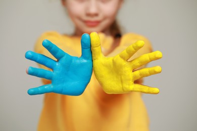 Photo of Little girl with hands painted in Ukrainian flag colors against light grey background, closeup. Love Ukraine concept