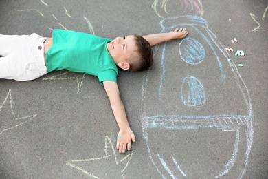 Little child lying near chalk drawing of rocket on asphalt