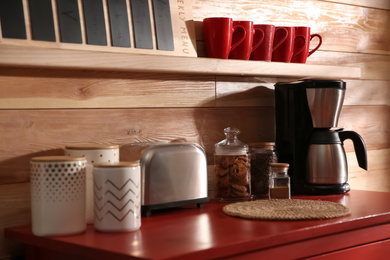 Photo of Modern coffeemaker and toaster on red table near wooden wall