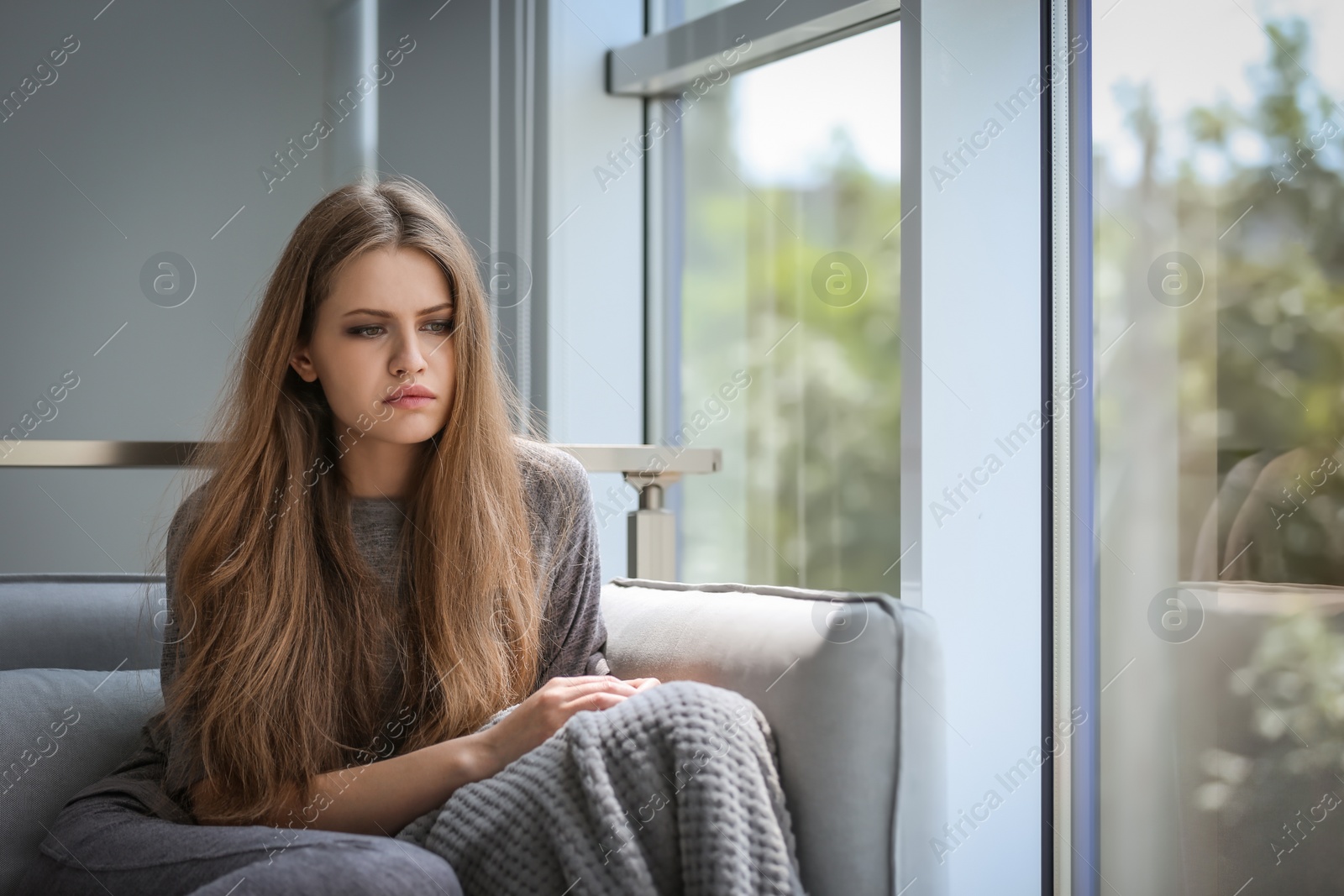 Photo of Depressed young woman sitting on sofa at home