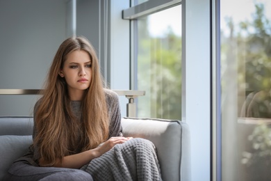 Depressed young woman sitting on sofa at home