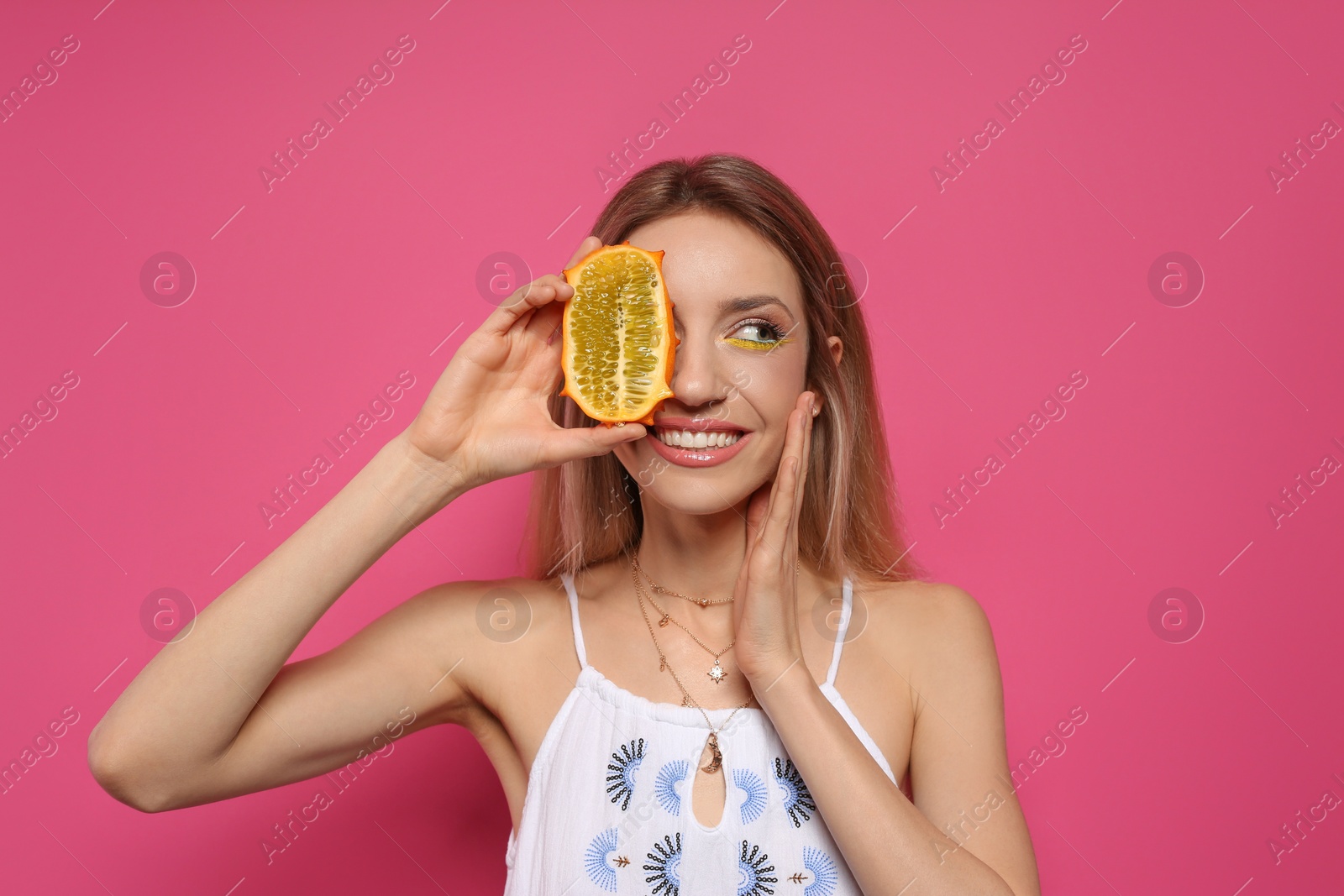 Photo of Young woman with fresh kiwano on pink background. Exotic fruit