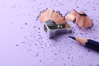 Photo of Blue pencil, shavings, crumbs and sharpener on violet background, closeup. Space for text