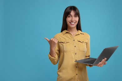 Special promotion. Happy woman with laptop pointing at something on light blue background, space for text