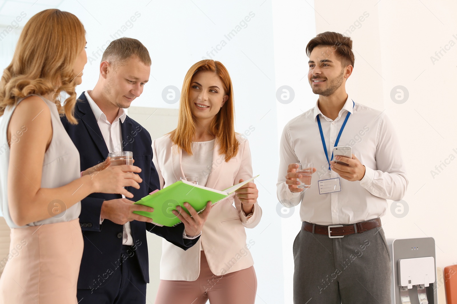 Photo of Co-workers having meeting near water cooler at workplace