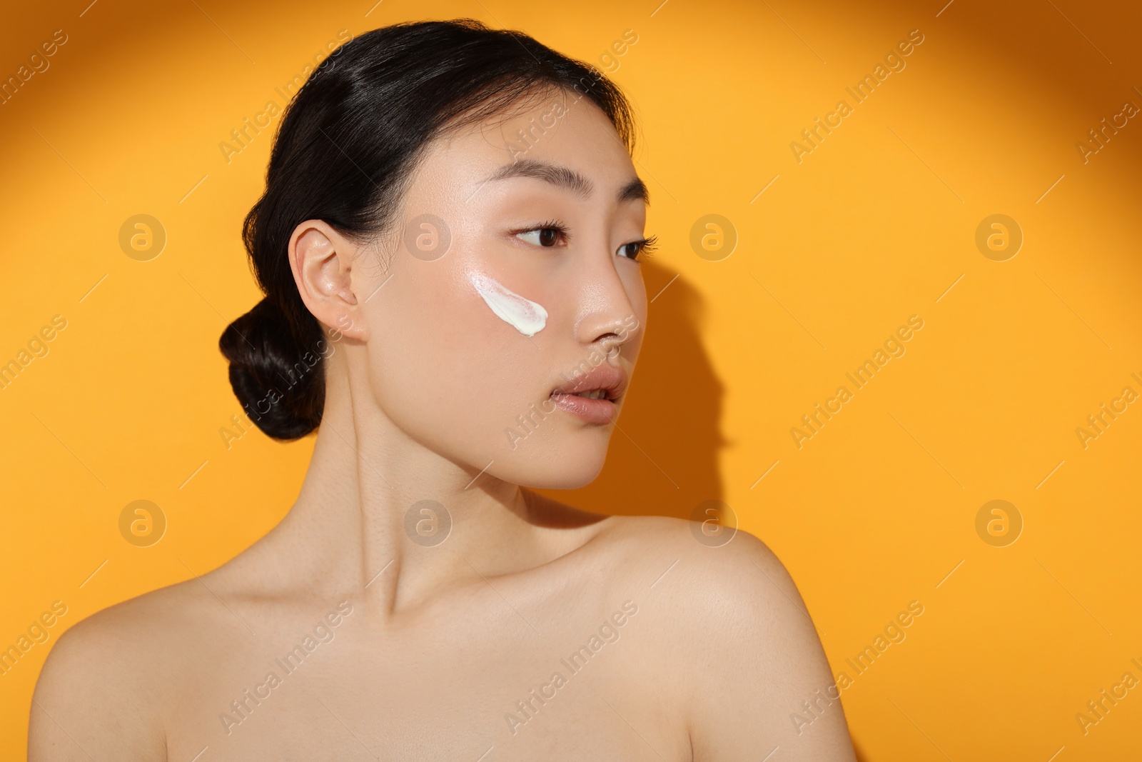 Photo of Beautiful young woman in sunlight with sun protection cream on her face against orange background, space for text