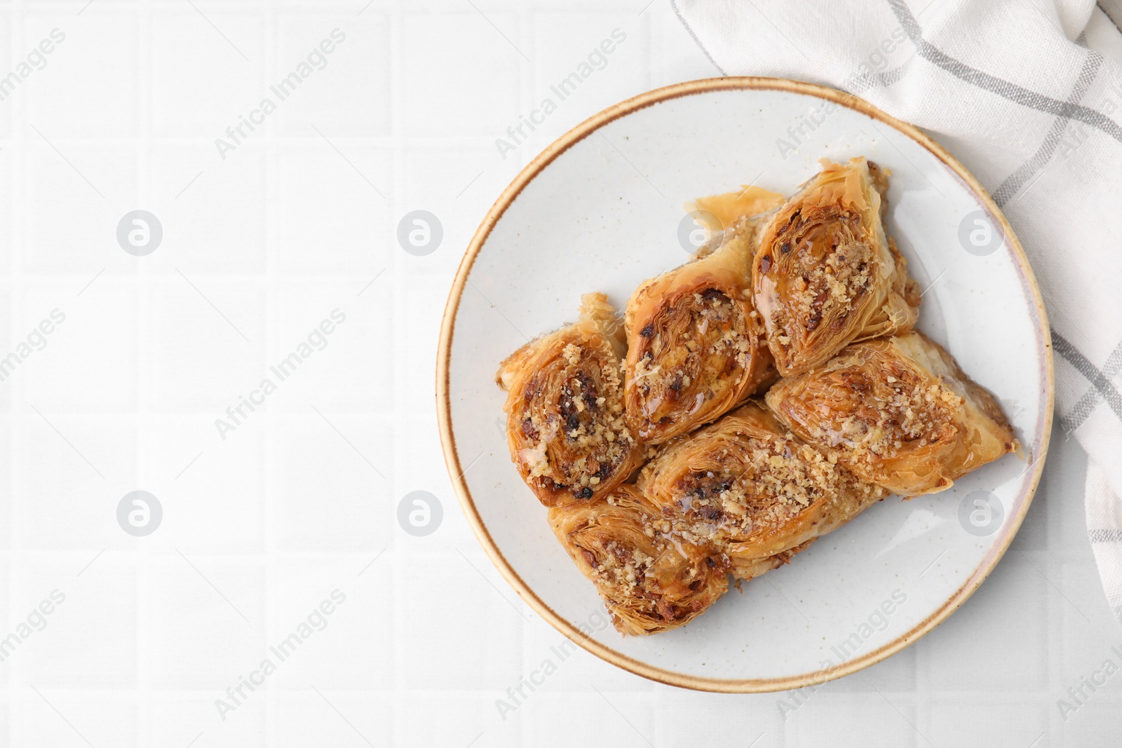 Photo of Eastern sweets. Pieces of tasty baklava on white tiled table, top view. Space for text