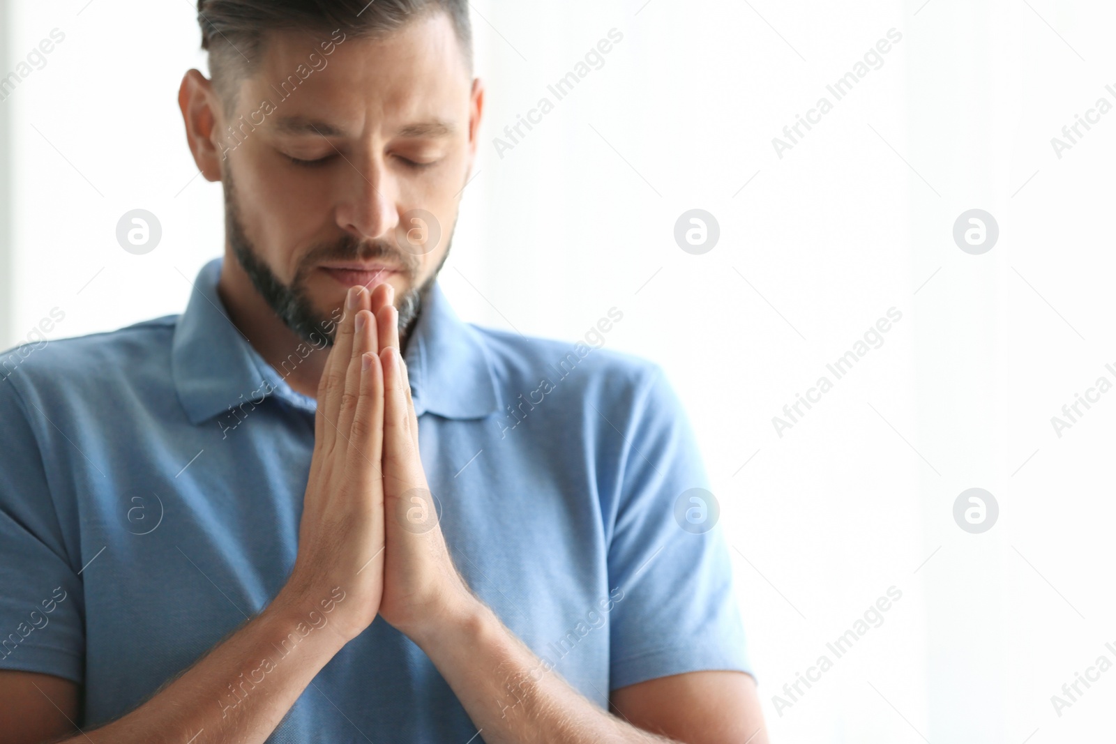 Photo of Man with hands clasped together for prayer on light background. Space for text