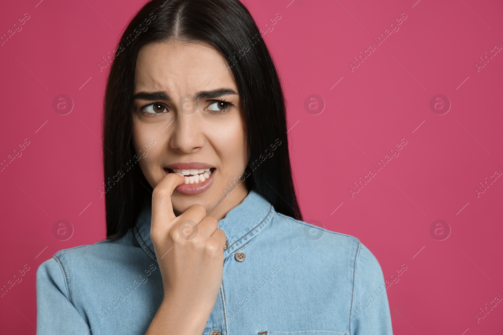 Photo of Young woman biting her nails on pink background. Space for text