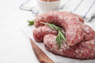 Photo of Raw homemade sausages and rosemary on white table, closeup. Space for text
