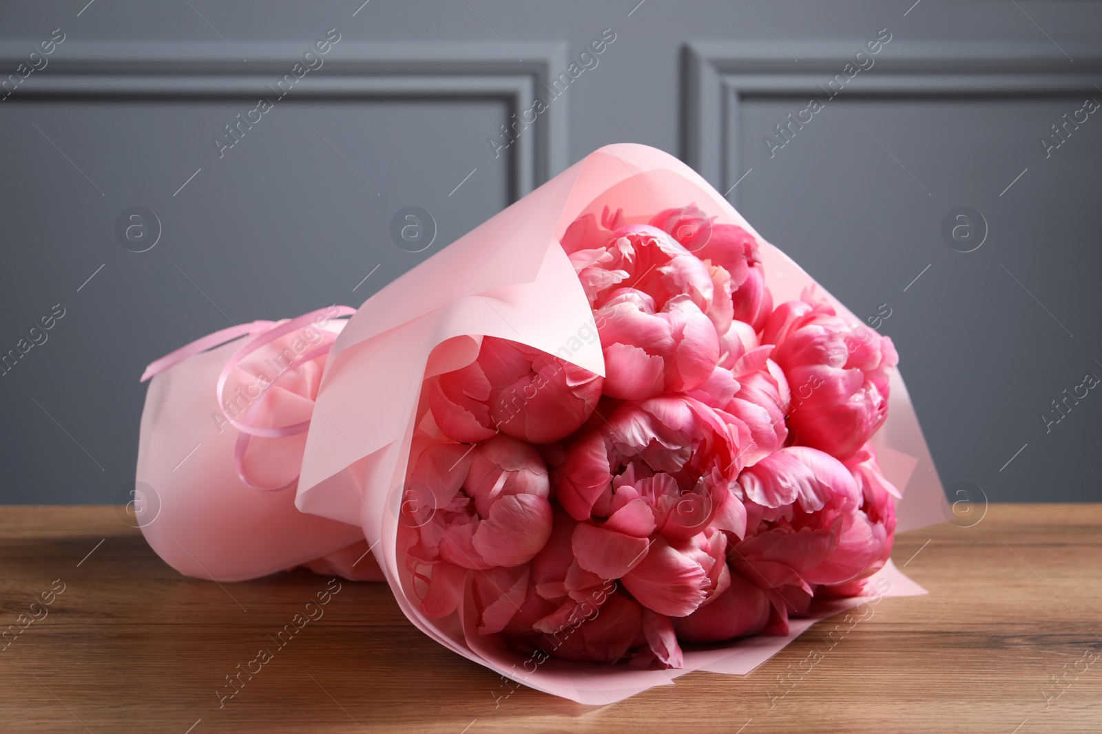 Photo of Bouquet of beautiful pink peonies on wooden table near grey wall