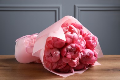 Bouquet of beautiful pink peonies on wooden table near grey wall