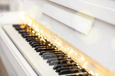 Photo of Glowing fairy lights on piano keys, closeup. Christmas music