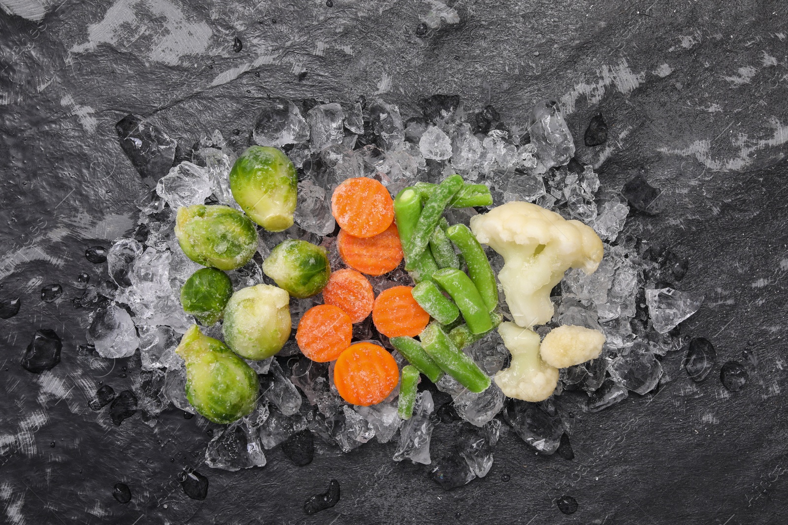 Photo of Different frozen vegetables and ice on black table, flat lay