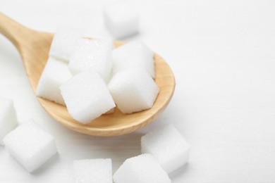 Photo of Many sugar cubes and wooden spoon on white table, closeup. Space for text
