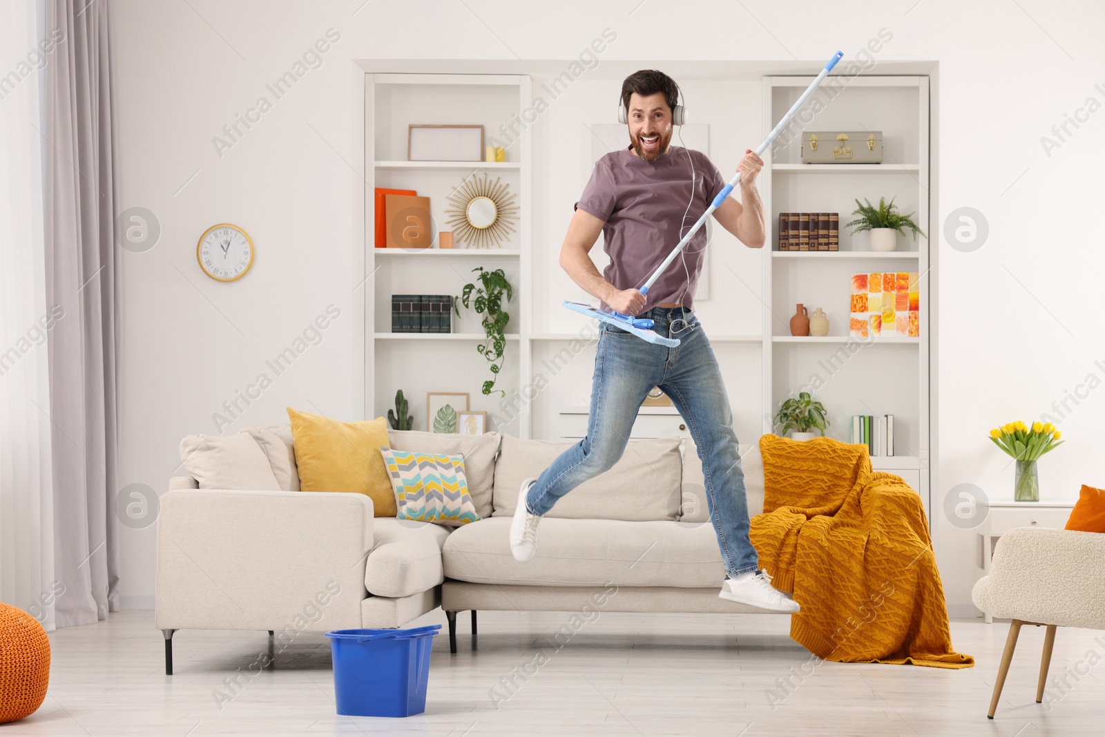 Photo of Spring cleaning. Man in headphones with mop singing while tidying up living room