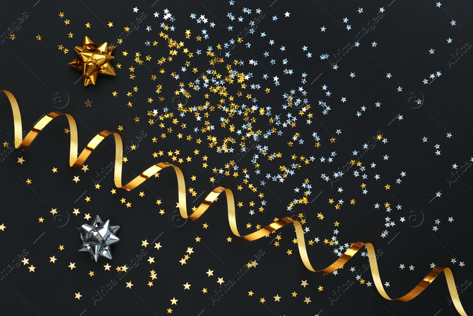 Photo of Confetti stars, gold streamer and bows on black background, flat lay. Christmas celebration