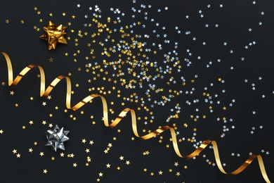 Photo of Confetti stars, gold streamer and bows on black background, flat lay. Christmas celebration