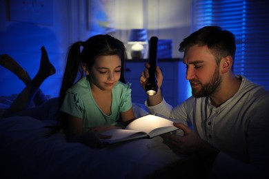Photo of Father with little daughter reading fairy tale in dark bedroom
